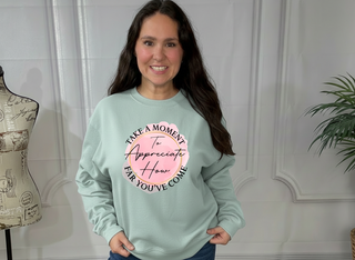 Woman wearing a light green sweatshirt with a motivational quote, standing in a room with a mannequin and plant.